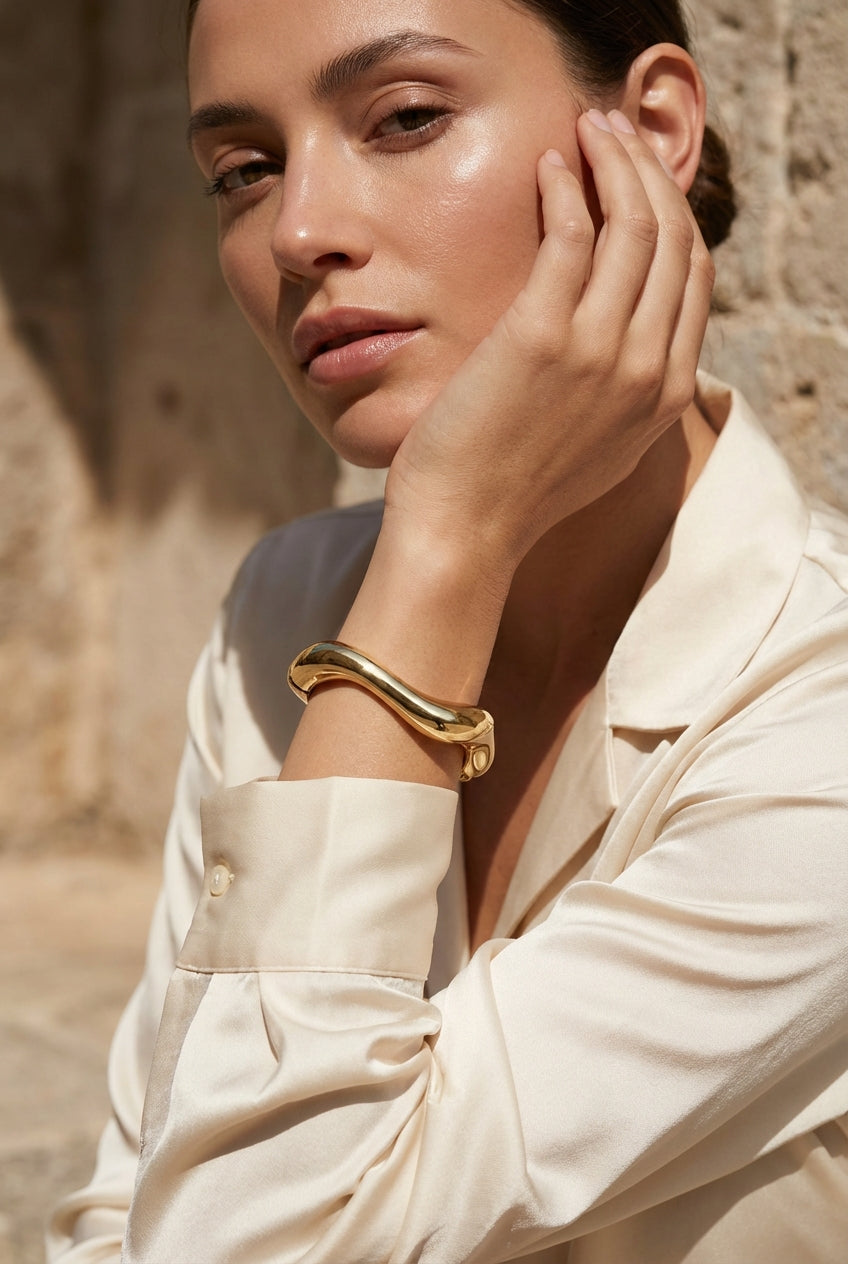 Sculptural gold wave‑form bracelet with spring hinged opening