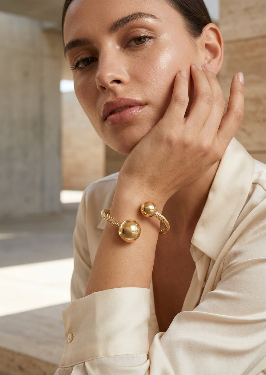 Gold open‑cuff bracelet with twin polished sphere ends and a twisted band